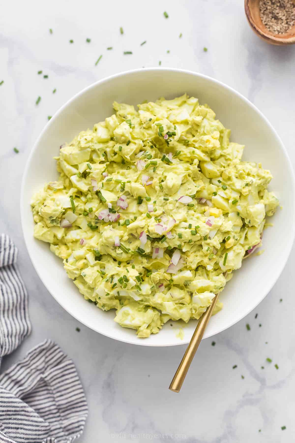 This Avocado Egg Salad is a healthy & satisfying salad made with less mayo! It's perfect for breakfast or lunch. a bowl of egg salad with red onion and chive garnish