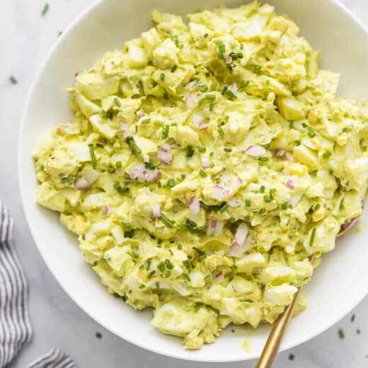 a bowl of egg salad with red onion and chive garnish