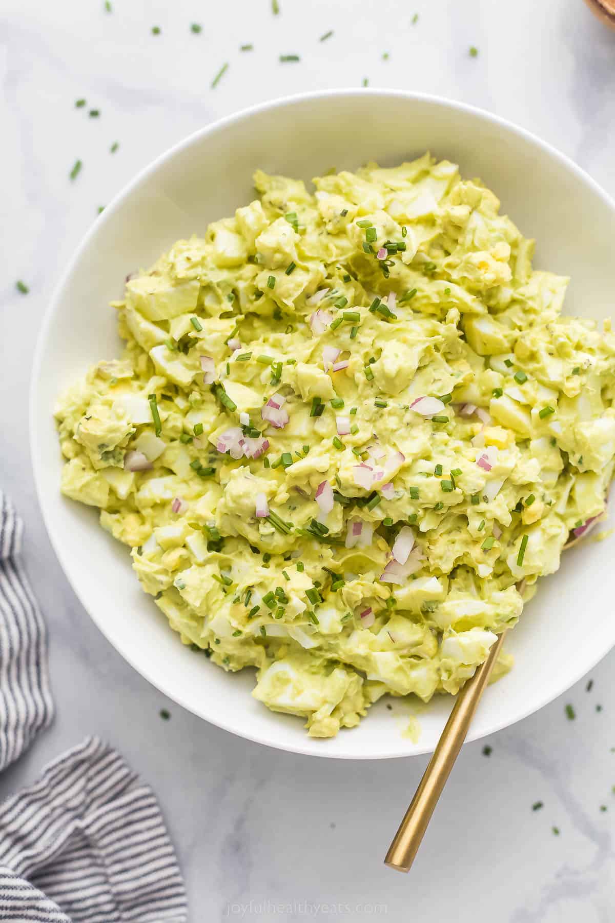 This Avocado Egg Salad is a healthy & satisfying salad made with less mayo! It's perfect for breakfast or lunch. a bowl of egg salad with red onion and chive garnish