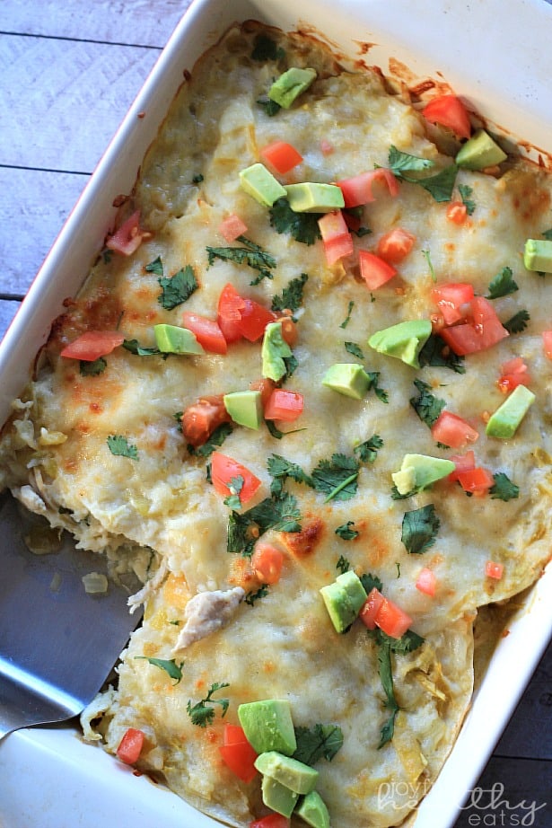 Top view of a baking dish of Chicken Enchilada Casserole topped with diced tomato and avocado with one serving removed