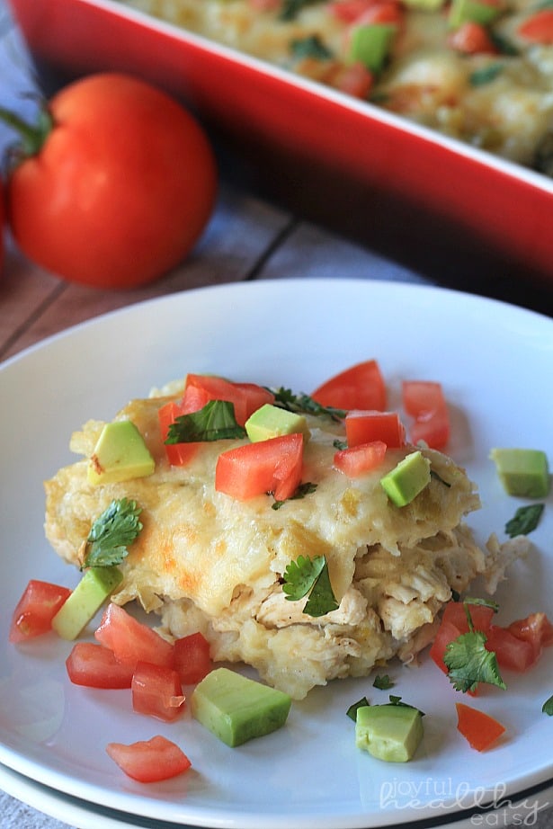 A serving of Chicken Enchilada Casserole on a plate topped with fresh herbs, diced tomato and avocado