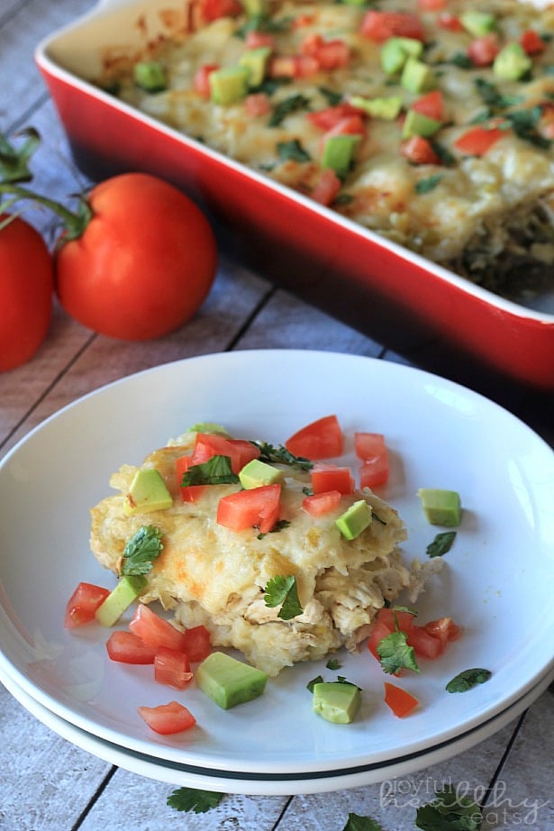 A serving of Chicken Enchilada Casserole on a plate topped with diced tomatoes and avocado