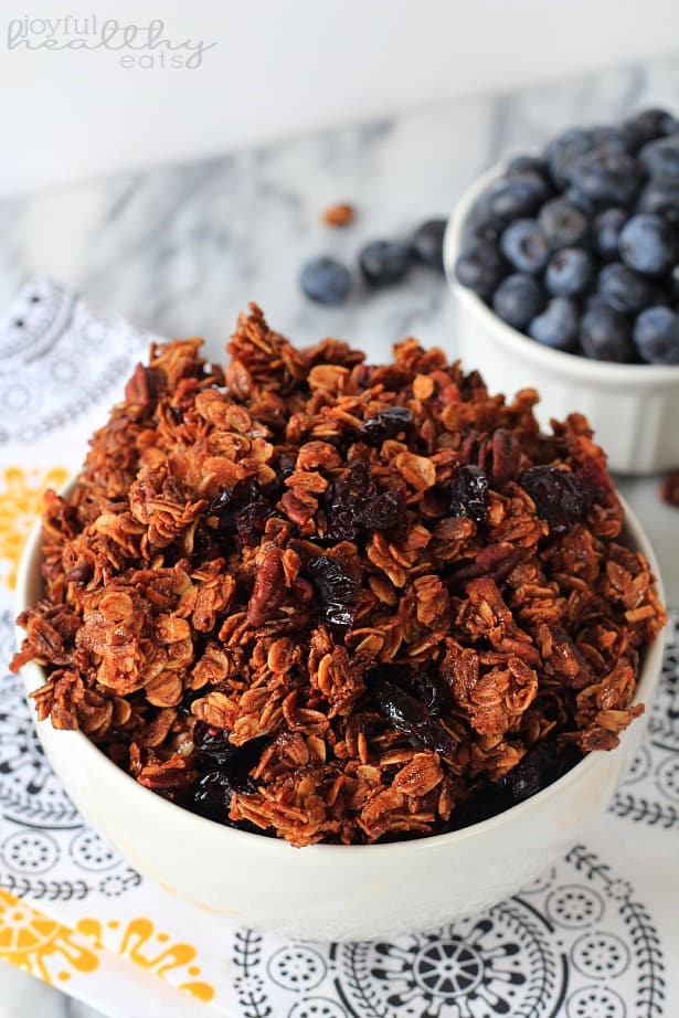 Top view of a bowl of Coconut Blueberry Pecan Granola next to a ramekin of fresh blueberries