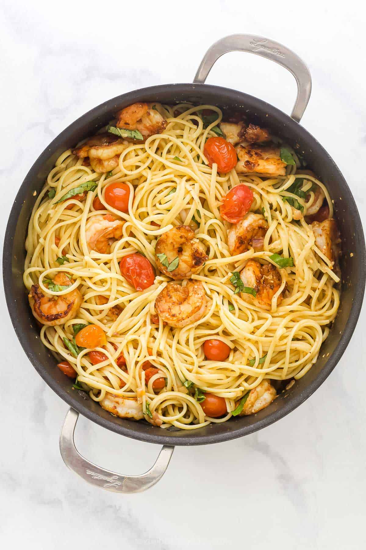 This Spicy Shrimp Pasta is light and flavorful thanks to the addition of blistered cherry tomatoes and fresh basil. A 30-minute dinner! Overhead view of spicy shrimp pasta in pan