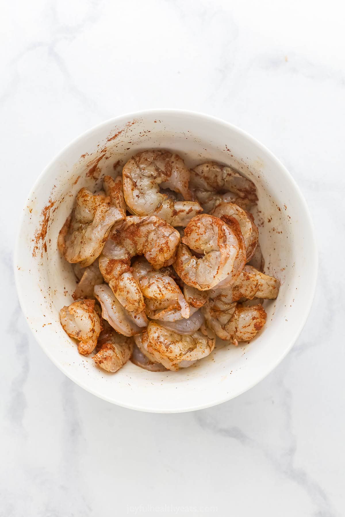 This Spicy Shrimp Pasta is light and flavorful thanks to the addition of blistered cherry tomatoes and fresh basil. A 30-minute dinner! Overhead view of uncooked shrimp tossed in bowl with seasoning