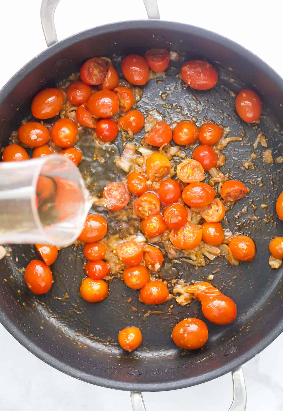 This Spicy Shrimp Pasta is light and flavorful thanks to the addition of blistered cherry tomatoes and fresh basil. A 30-minute dinner! Overhead view of wine being poured into skillet of cherry tomatoes