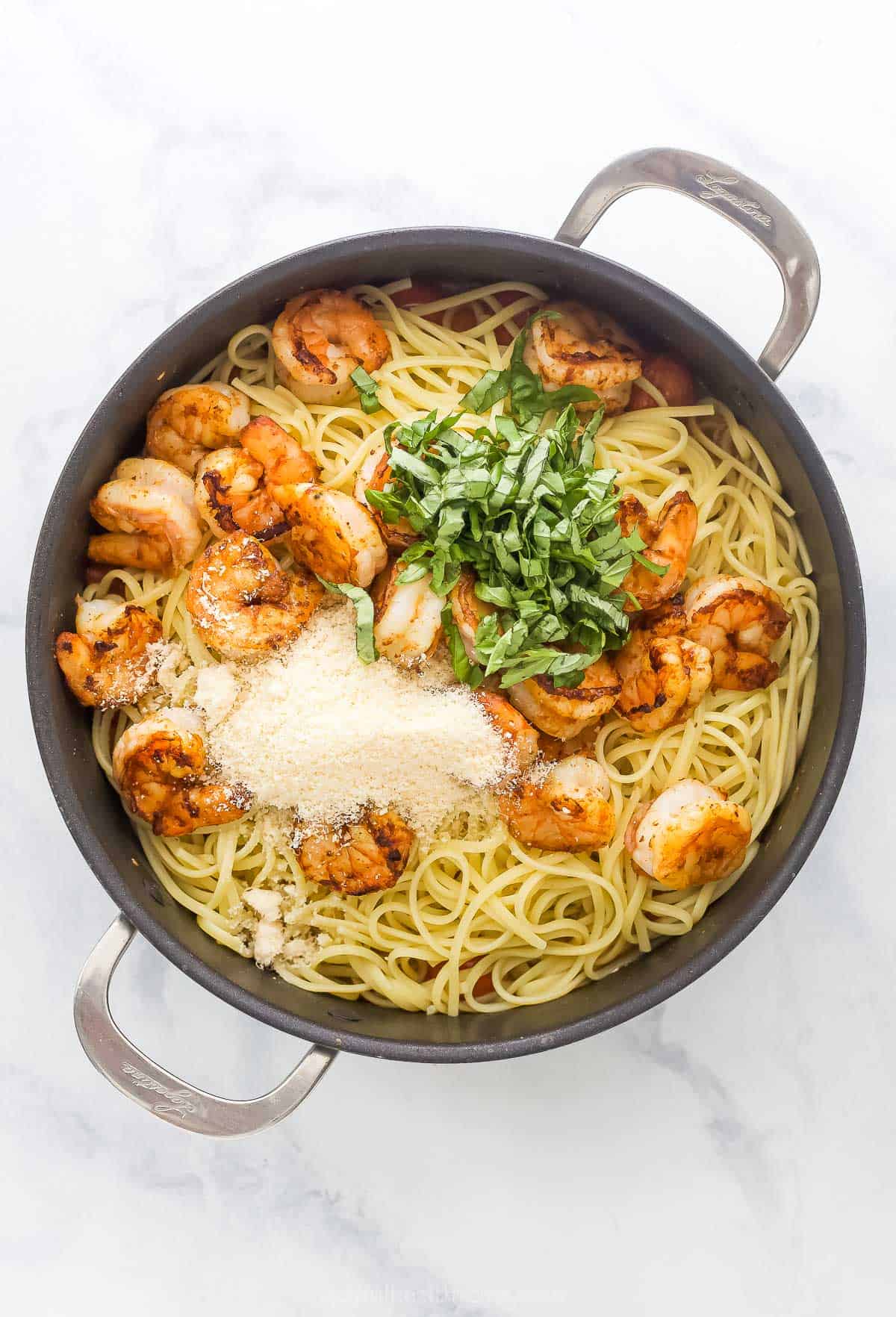 This Spicy Shrimp Pasta is light and flavorful thanks to the addition of blistered cherry tomatoes and fresh basil. A 30-minute dinner! Overhead view of basil and parmesan added to pan of spicy shrimp pasta