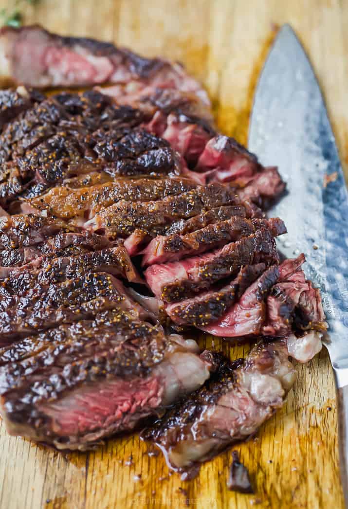 A seared ribeye sliced into thin pieces on a cutting board with a large knife