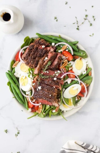 A plate of steak salad on a marble countertop with a dish of dressing beside it