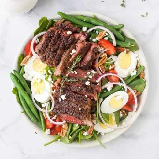 A plate of steak salad on a marble countertop with a dish of dressing beside it