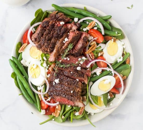 A plate of steak salad on a marble countertop with a dish of dressing beside it