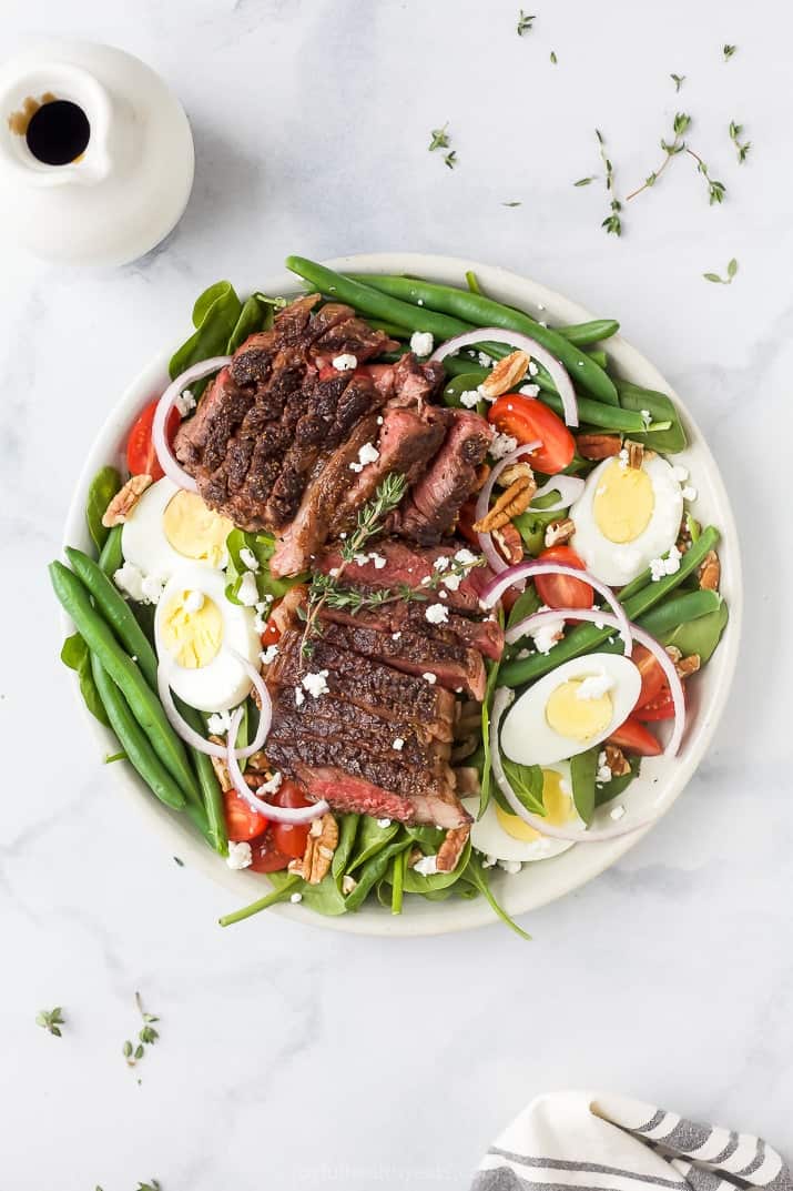 A plate of steak salad on a marble countertop with a dish of dressing beside it