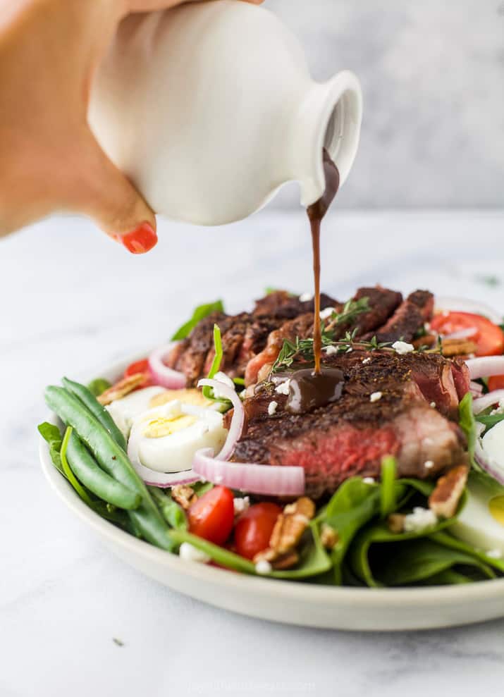 Homemade balsamic dressing being poured over a freshly-made salad on a plate