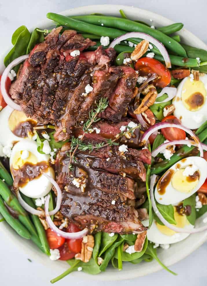A close-up shot of a steak salad with hard-boiled eggs, goat cheese and baby spinach