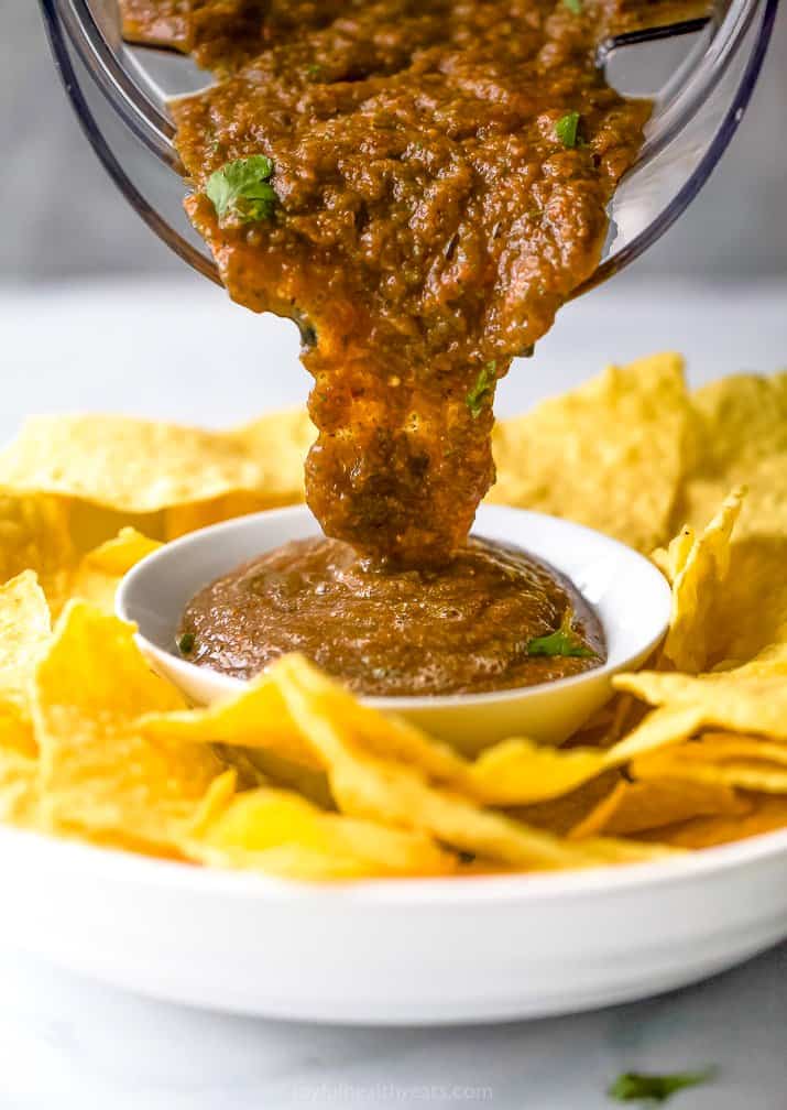 Pouring salsa into a bowl surrounded by chips