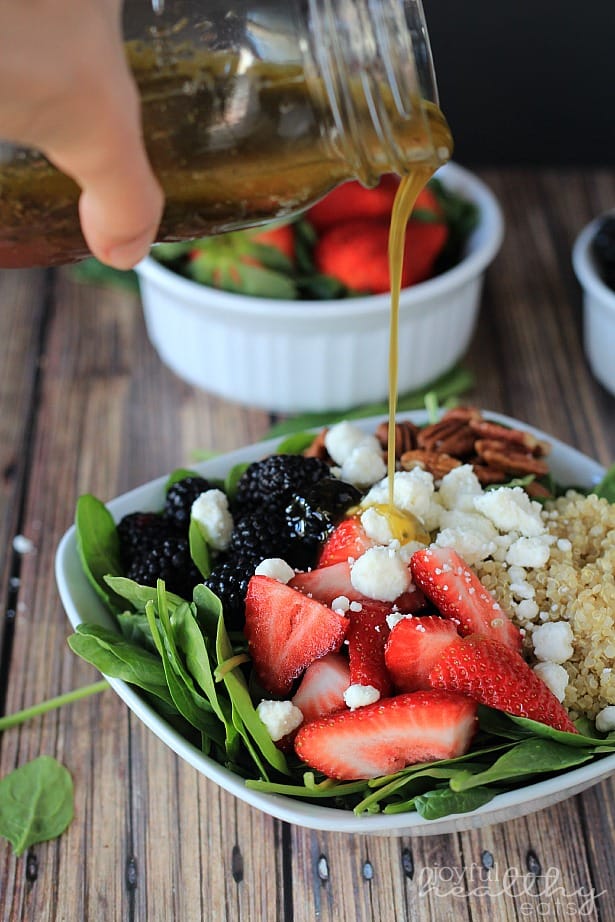 Detox Berry Quinoa Spinach Salad in a bowl being drizzled with honey vinaigrette