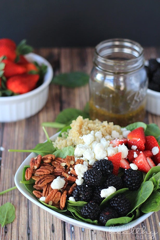Detox Berry Quinoa Spinach Salad in a bowl next to a jar of homemade vinaigrette