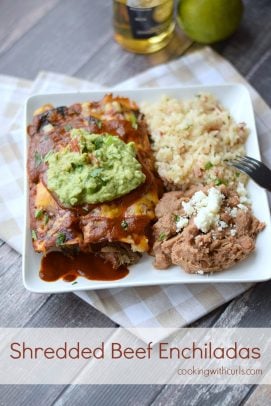 Shredded beef enchiladas topped with guacamole on a plate with rice and refried beans