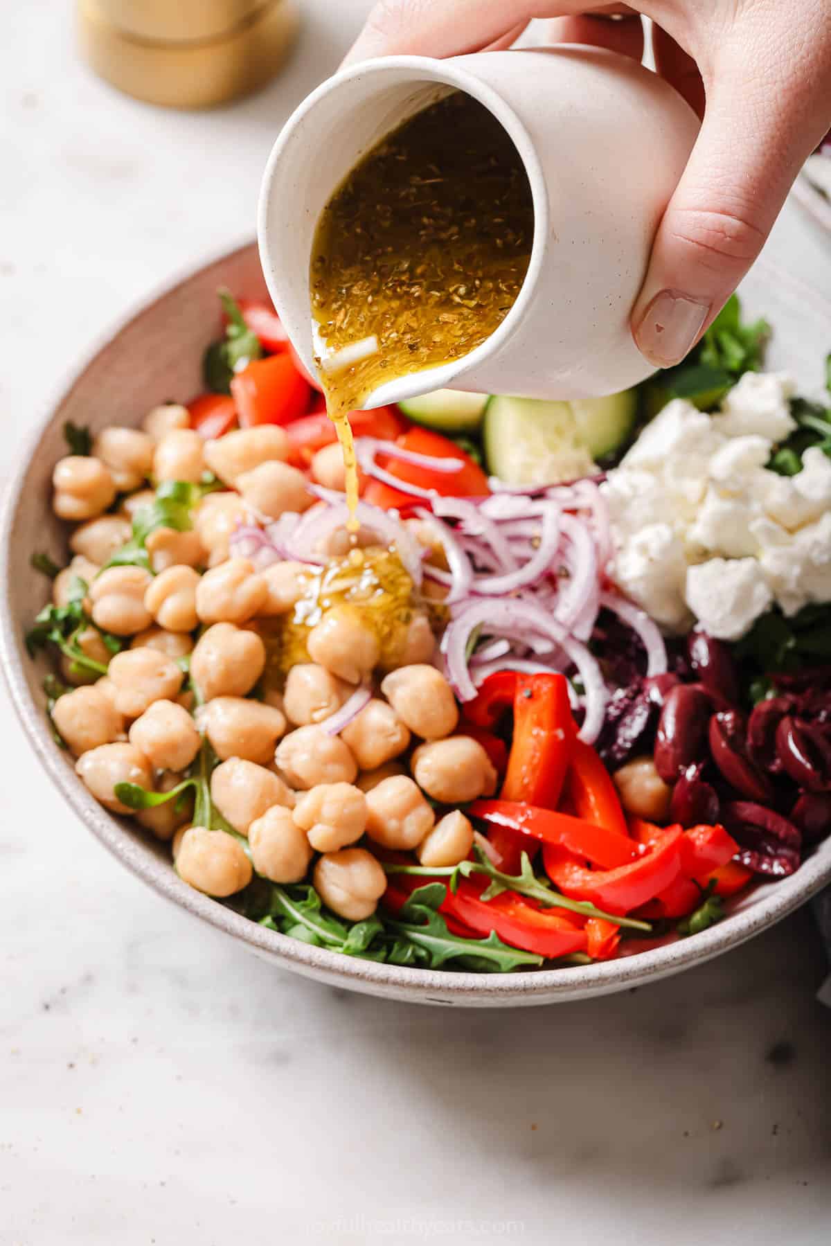 Pouring vinaigrette over the Mediterranean salad.