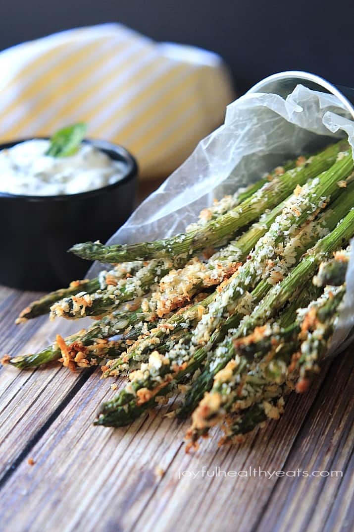 Baked Asparagus Fries in wax paper with a bowl of Garlic Herb Aioli