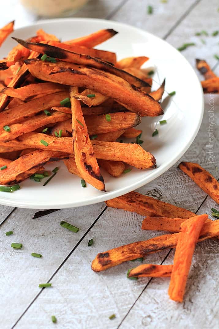 A plate of sweet potato fries on a table with a few loose fries beside the plate