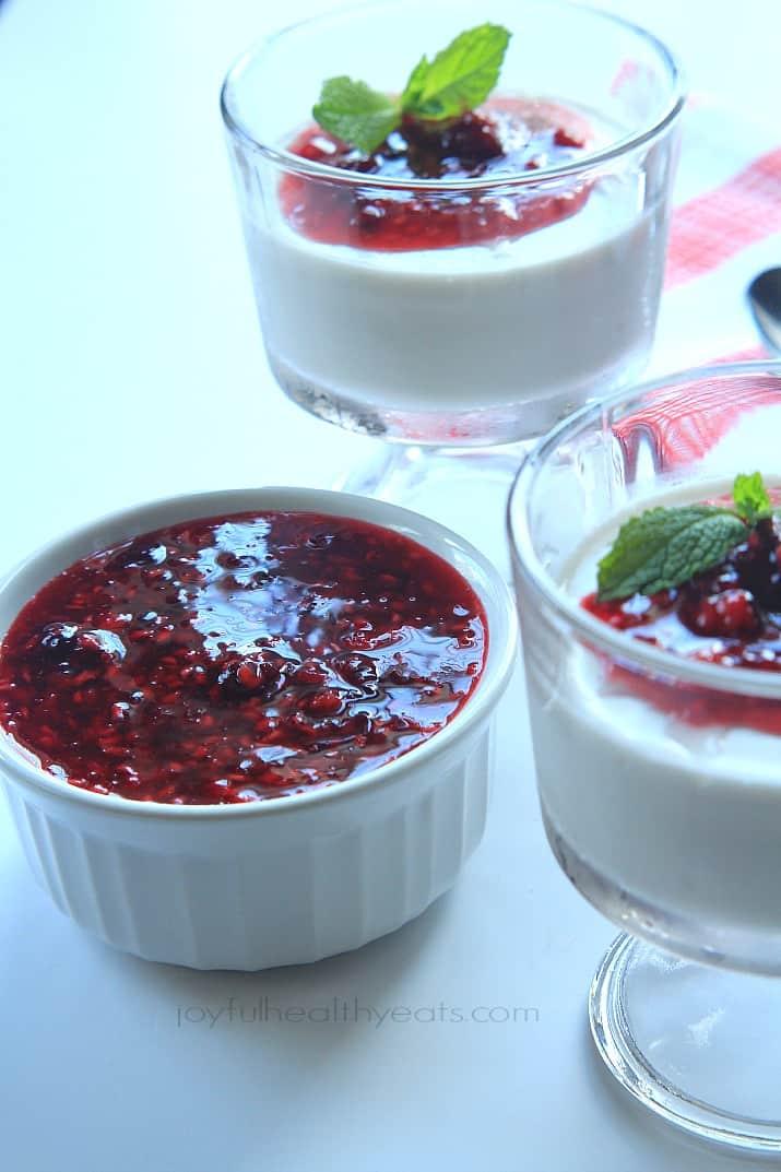 Coconut Panna Cotta topped with Raspberry Blackberry Compote in dessert glasses next to a ramekin of compote