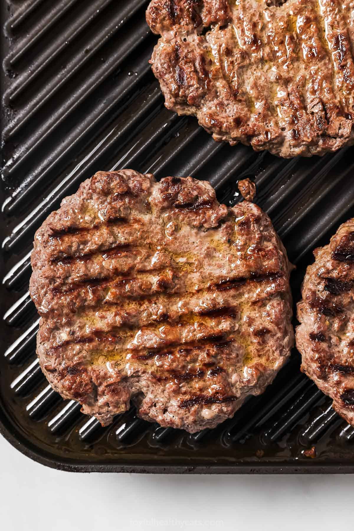These Cowboy Hamburger Sliders are topped with creamy avocado, balsamic caramelized onions, and crispy bacon. Always a crowd-pleaser! Overhead view of slider patties on grill pan