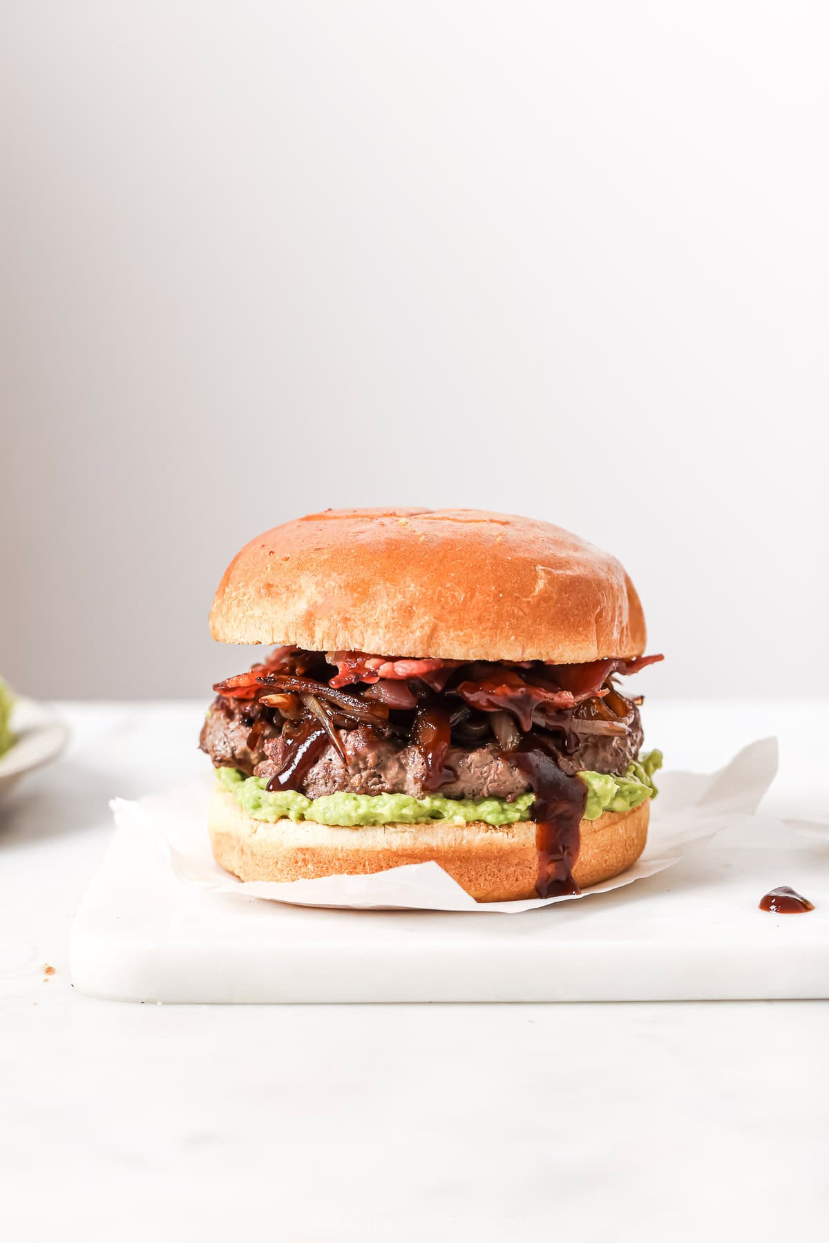 These Cowboy Hamburger Sliders are topped with creamy avocado, balsamic caramelized onions, and crispy bacon. Always a crowd-pleaser! Homemade cowboy hamburger slider on parchment square