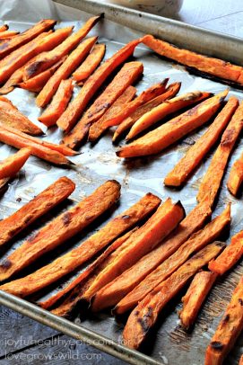 Crispy baked sweet potato fries lined up on a large metal baking sheet lined with parchment paper.
