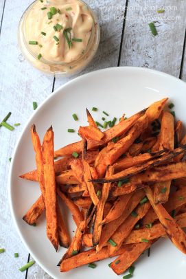 An overhead shot of a plate of sweet potato fries and a jar of chipotle aioli on a wooden table