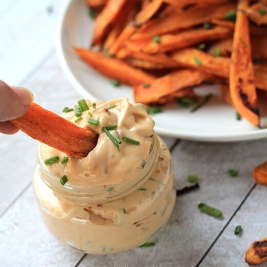 A crispy oven-baked sweet potato fry being dipped into a jar of homemade aioli