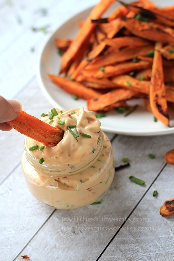 A crispy oven-baked sweet potato fry being dipped into a jar of homemade aioli