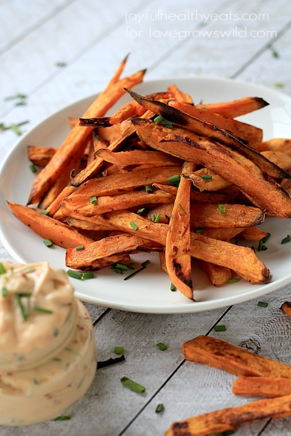 Sweet potato fries piled onto a plate with a small jar full of chipotle lime sauce in the foreground