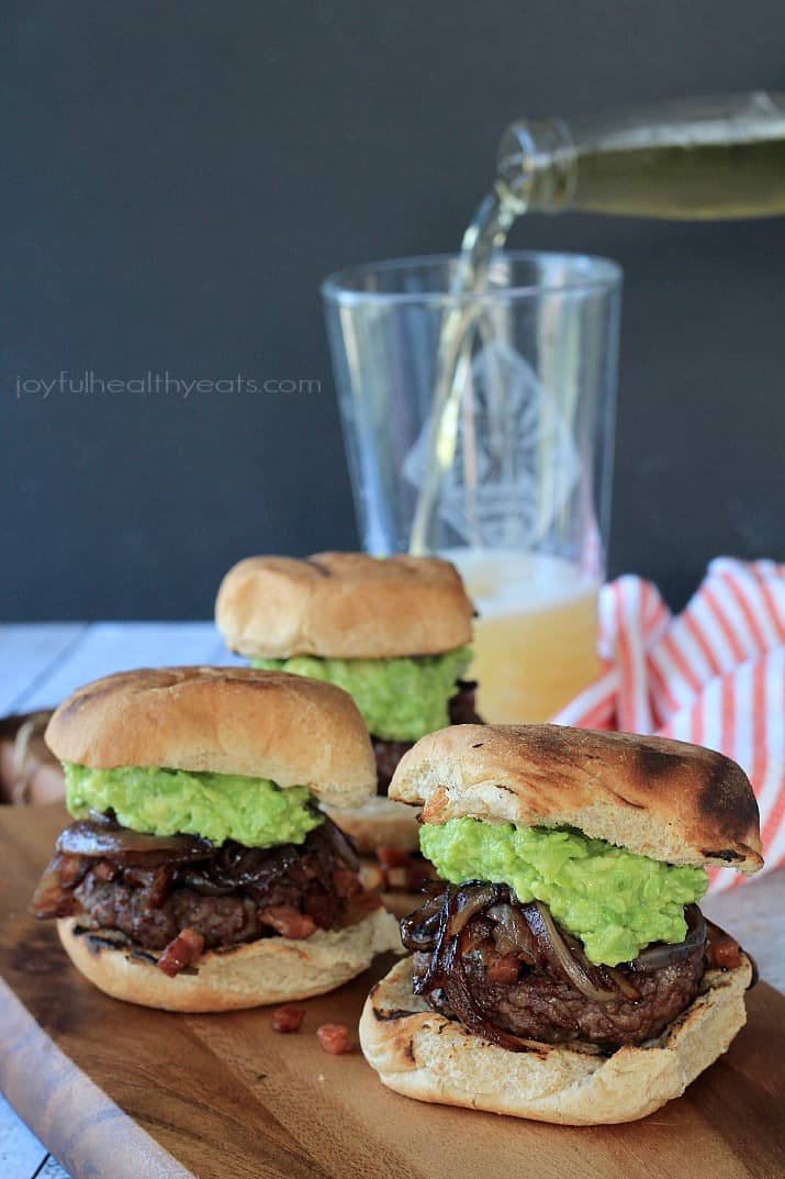 Three Gourmet "Cowboy" Slider burgers on a wooden board next to a pint of beer