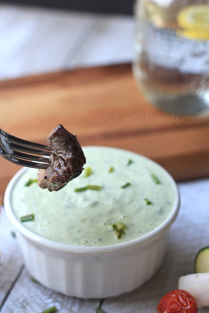 A piece of grilled beef being dipped in Avocado Cucumber Tzatziki