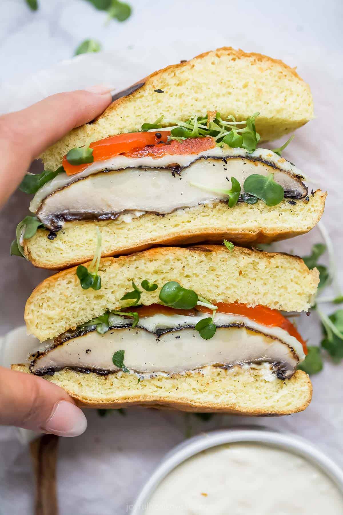 Melti provolone, roasted red pepper and creamy trafle IOli, it can only be the best portobelo mushroom sandwich! Hands hold two half of a portobelo mushroom sandwich