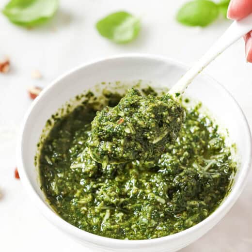Spoonful of homemade basil pesto held over bowl