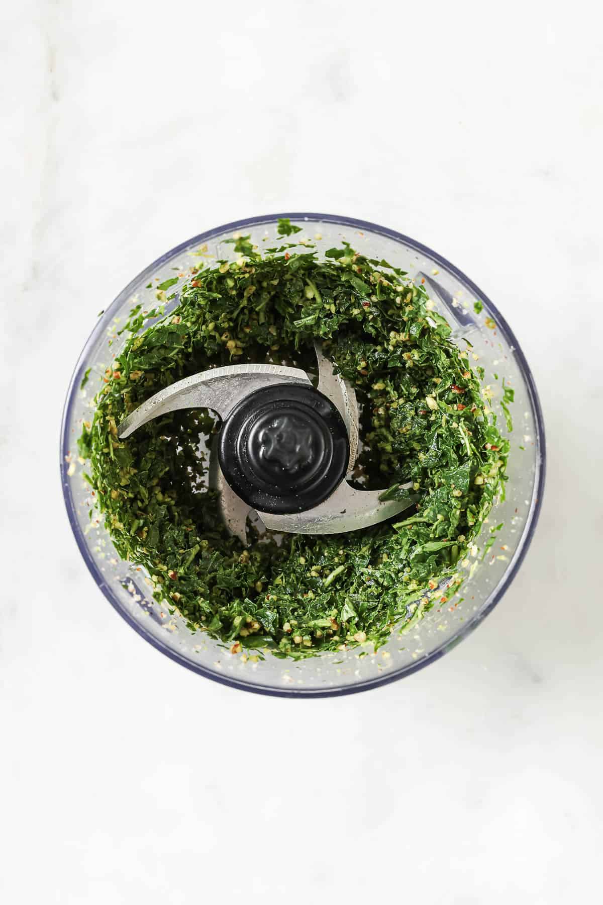 This Homemade Basil Pesto recipe is made with pecans instead of pine nuts to give it some extra body. It's my favorite way to make pesto! Chopped basil, nuts, and other ingredients for pesto in food processor bowl