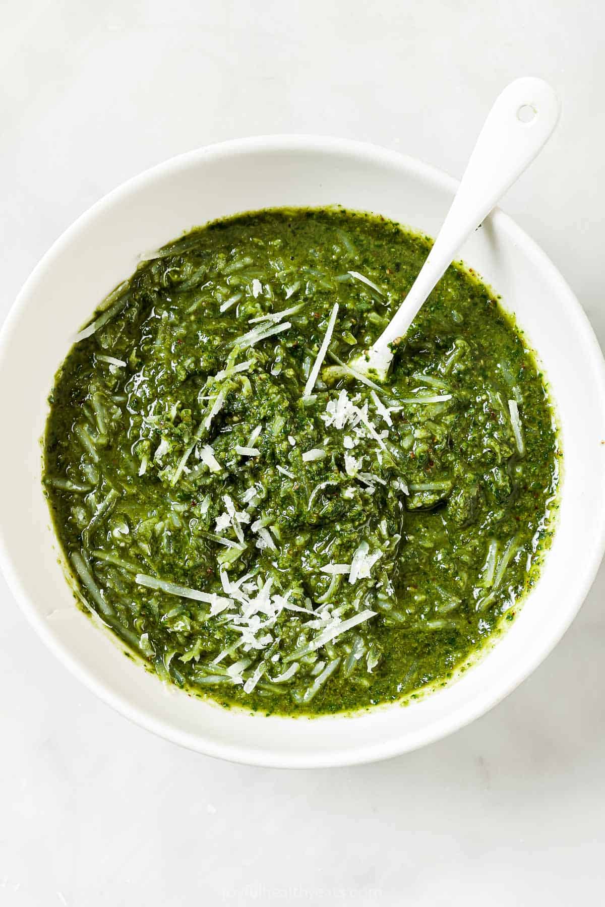 This Homemade Basil Pesto recipe is made with pecans instead of pine nuts to give it some extra body. It's my favorite way to make pesto! Stirring Parmesan into bowl of homemade basil pesto