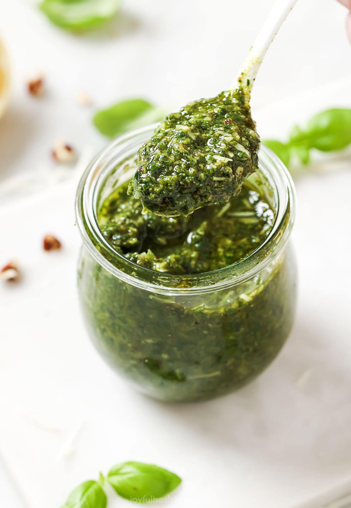 This Homemade Basil Pesto recipe is made with pecans instead of pine nuts to give it some extra body. It's my favorite way to make pesto! Spoonful of homemade basil pesto held over jar
