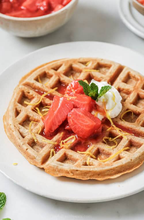 Crispy oatmeal waffle on plate with strawberry compote and whipped cream