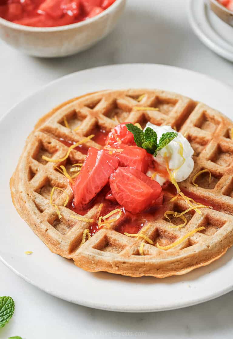 Crispy oatmeal waffle on plate with strawberry compote and whipped cream