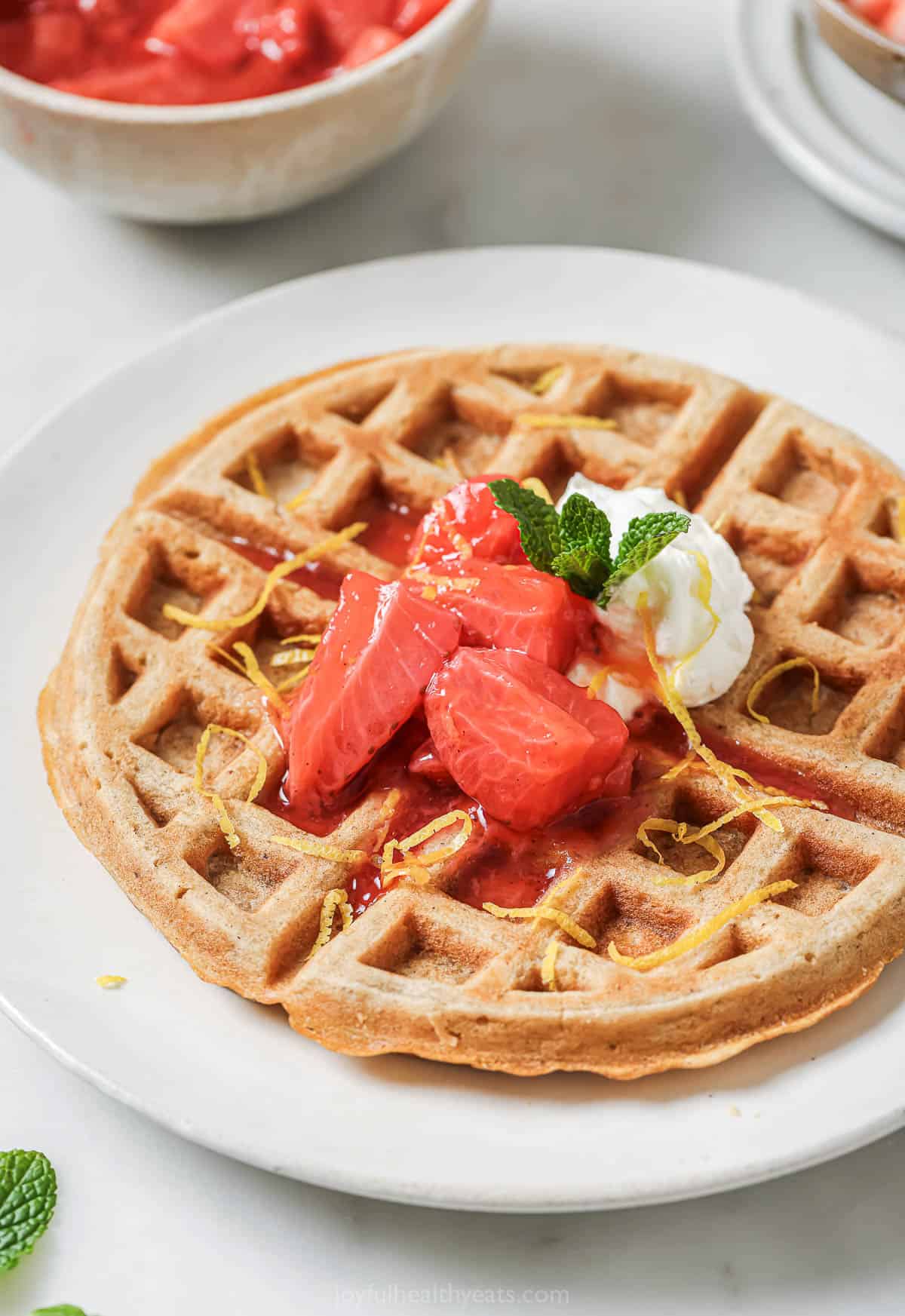 These oatmeal waffles are a delicious start to any morning! They’re crispy on the outside, fluffy on the inside, and all around perfect! Crispy oatmeal waffle on plate with strawberry compote and whipped cream