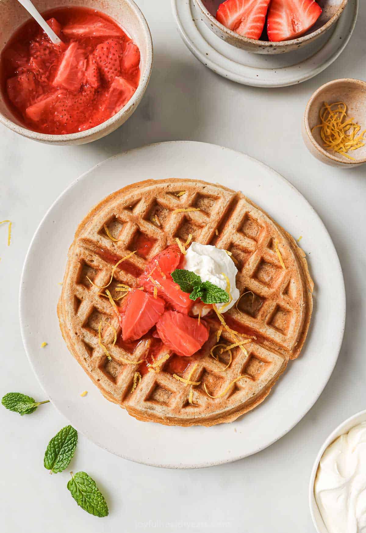 Overhead view of oatmeal waffle on plate with strawberry compote and whipped cream