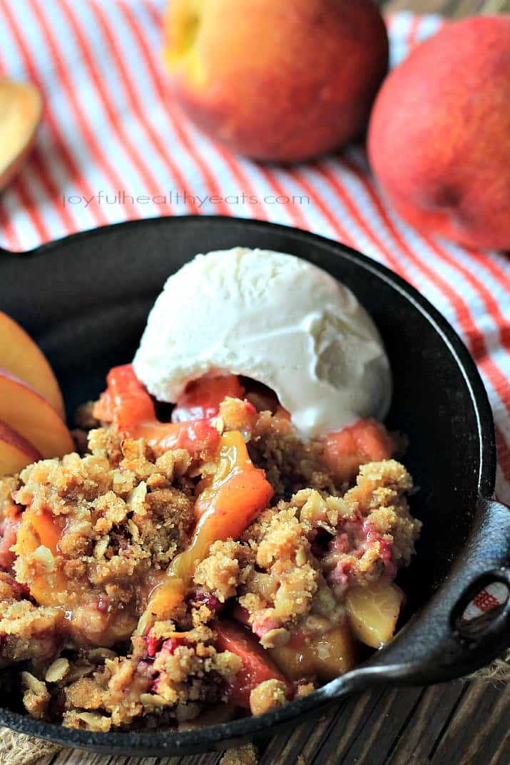 a skillet with raspberry peach cobbler and oatmeal crumble with ice cream on the side 