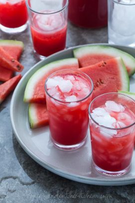 Two glasses of watermelon raspberry lemonade on a plate with watermelon slices
