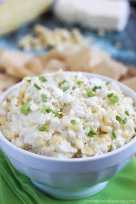 A white bowl of cheesy corn dip topped with fresh herbs
