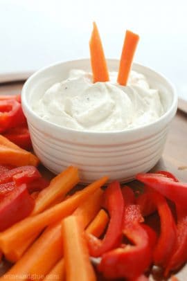 A white bowl of creamy veggie dip with carrot and red bell pepper slices