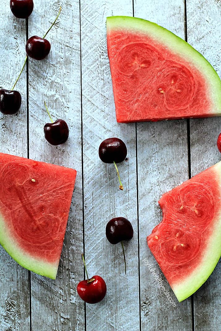 Top view of watermelon wedges and fresh cherries on a wooden board