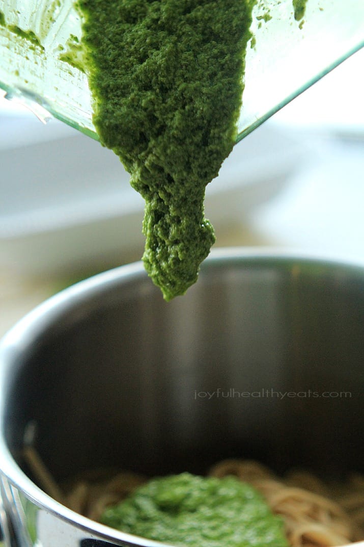 Pesto being added to pasta in a bowl